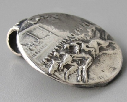 “Ahead By A Nose” 1" diameter, Price: $189, Chisholm Ref. #: S-SH2 - This silver piece captures the excitement of a close horse race. Horses and jockeys vie for position in the foreground. Behind them spectators crowd the rail with the grandstand rising in the background. Handcrafted in .960 silver.