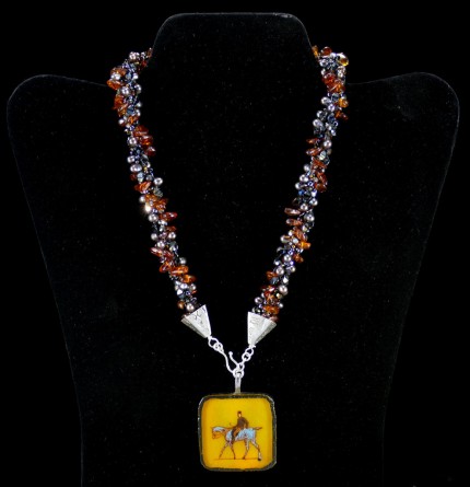 “Ambling Along Silver & Beadwork Necklace” Pendant: 1.5" square, Overall length: 18", Price: $650, Chisholm Ref #: SBW-N1 - This one-of-a-kind, beaded necklace is made of amber, freshwater pearls, fire polished Czech crystals, and Japanese square & ring shaped glass beads. The handmade silver bead caps show the imprint of many warmblood breed logos. The focal piece is a hand-painted, fused glass pendant featuring a relaxed rider ambling along.