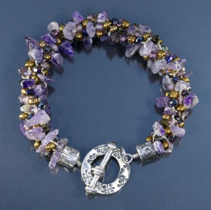 “Amethyst Dream Bracelet” Overall Length 8.75", Price: $329, Chisholm Ref. #: SB-108 - One of a kind beaded bracelet woven with amethyst, glass, and Czech crystal beads. The end caps have a swirling texture, the toggle clasp bears the warmblood breed logos, and the closure is set with two garnets cabuchons. Findings are hancrafted in .960 silver.