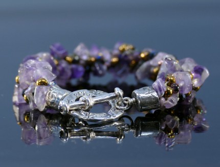 “Amethyst Dream Bracelet” Overall Length 8.75", Price: $329, Chisholm Ref. #: SB-108 - One of a kind beaded bracelet woven with amethyst, glass, and Czech crystal beads. The end caps have a swirling texture, the toggle clasp bears the warmblood breed logos, and the closure is set with two garnets cabuchons. Findings are hancrafted in .960 silver.