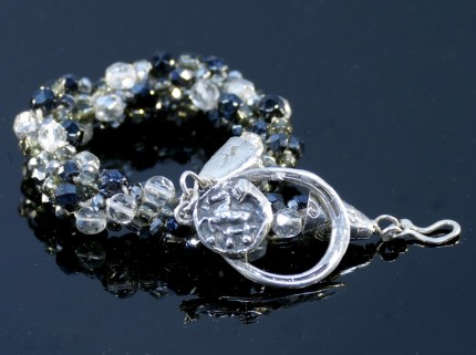 “Farriers’ Art Bracelet” Overall length: 8.5", Price: $329, Chisholm Ref. #: SB-109 - One of a kind beaded bracelet made with fire polished Czech crystyals, vintage crystals, and glass sead beads in shades of black, silver, and clear. The clasp combines two horseshoe motifs: the main part of the clasp, to which the hook attaches, is shaped like a horseshoe. Adorning the clasp is a small horse emerging from a curved horse shoe nail. Findings handcrafted in .960 silver.