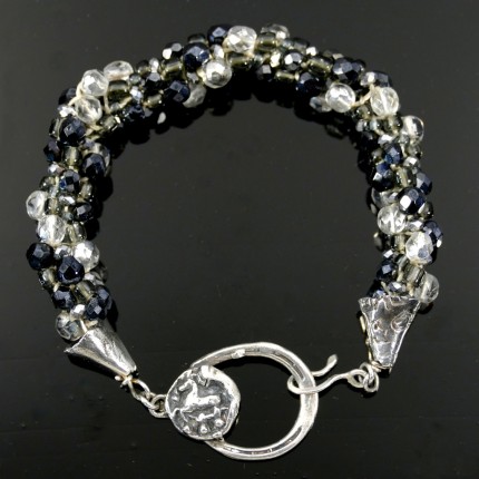 “Farriers’ Art Bracelet” Overall length: 8.5", Price: $329, Chisholm Ref. #: SB-109 - One of a kind beaded bracelet made with fire polished Czech crystyals, vintage crystals, and glass sead beads in shades of black, silver, and clear. The clasp combines two horseshoe motifs: the main part of the clasp, to which the hook attaches, is shaped like a horseshoe. Adorning the clasp is a small horse emerging from a curved horse shoe nail. Findings handcrafted in .960 silver.