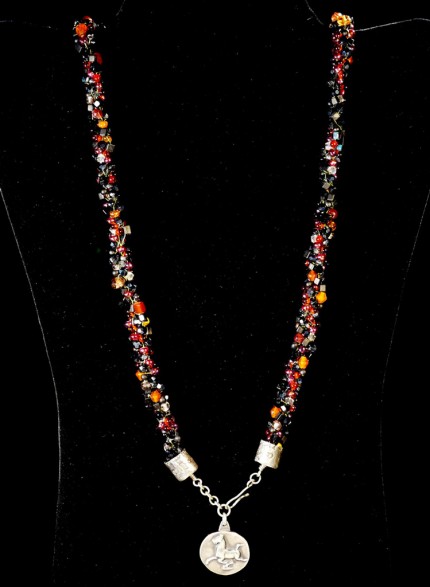 “Flying Horse Beaded Necklace” Overall length: 28.5", Flying Horse Pendant: 1" Diameter, Price: $600, Chisholm Ref. #: SBW-N4 | This one-of-a-kind silver & beadwork necklace woven using vintage glass beads and crystals, Czech fire polished crystals, and Japanese toho beads in shades of reds, orange and black. The end-caps are textured with warm blood breed logos. The focal piece features the classic Han Flying Horse. The findings are all handcrafted in .960 silver.