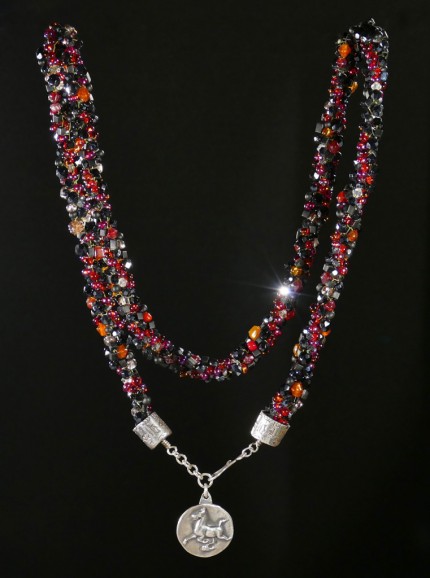 “Flying Horse Beaded Necklace” Overall length: 28.5", Flying Horse Pendant: 1" Diameter, Price: $600, Chisholm Ref. #: SBW-N4 | This one-of-a-kind silver & beadwork necklace woven using vintage glass beads and crystals, Czech fire polished crystals, and Japanese toho beads in shades of reds, orange and black. The end-caps are textured with warm blood breed logos. The focal piece features the classic Han Flying Horse. The findings are all handcrafted in .960 silver.