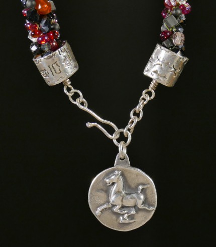 “Flying Horse Beaded Necklace” Overall length: 28.5", Flying Horse Pendant: 1" Diameter, Price: $600, Chisholm Ref. #: SBW-N4 | This one-of-a-kind silver & beadwork necklace woven using vintage glass beads and crystals, Czech fire polished crystals, and Japanese toho beads in shades of reds, orange and black. The end-caps are textured with warm blood breed logos. The focal piece features the classic Han Flying Horse. The findings are all handcrafted in .960 silver.