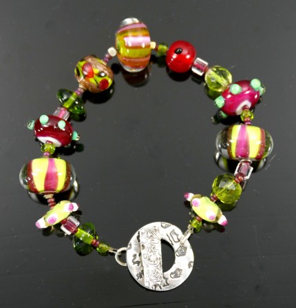 “Glowing Glass Bracelet” Overall length: 8.5", Price: $229, Chisholm Ref. #: SB-111 | One of a kind bracelet made with brilliant, lamp-worked, glass beads, vintage crystal, and glass seed beads. The round toggle clasp bears the logos of the major warmblood breeds. Findings handcrafted in .960 silver.