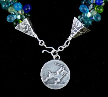 “Seafoam Polo Necklace” Overall length: 16", Polo pendant: 7/8" Diameter, Price: $550, Chisholm Ref. #: SBW-N10 | This one-of-a-kind silver & beadwork necklace is woven of glass beads: matte teardrops, Czech fire polished crystals, and seed bead, all in hues of the brilliant ocean. The silver end-caps are textured with wildflower leaves, and the focal piece features a polo player & pony both totally intent on the ball. The findings are all handcrafted in .960 silver.