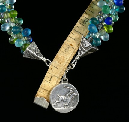 “Seafoam Polo Necklace” Overall length: 16", Polo pendant: 7/8" Diameter, Price: $550, Chisholm Ref. #: SBW-N10 | This one-of-a-kind silver & beadwork necklace is woven of glass beads: matte teardrops, Czech fire polished crystals, and seed bead, all in hues of the brilliant ocean. The silver end-caps are textured with wildflower leaves, and the focal piece features a polo player & pony both totally intent on the ball. The findings are all handcrafted in .960 silver.