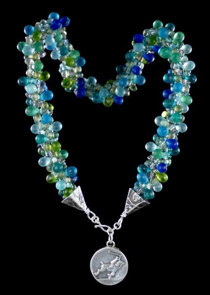 “Seafoam Polo Necklace” Overall length: 16", Polo pendant: 7/8" Diameter, Price: $550, Chisholm Ref. #: SBW-N10 | This one-of-a-kind silver & beadwork necklace is woven of glass beads: matte teardrops, Czech fire polished crystals, and seed bead, all in hues of the brilliant ocean. The silver end-caps are textured with wildflower leaves, and the focal piece features a polo player & pony both totally intent on the ball. The findings are all handcrafted in .960 silver.