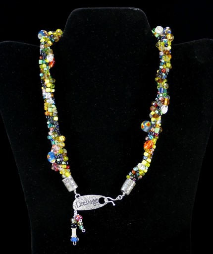 “Spirited Dressage Beaded Necklace” Overall length: 20", Clasp length: 2", Price: $550, Chisholm Ref. #: SBW-N9 | One-of-a-kind silver & beadwork necklace is woven using a multicolored “bead soup” made up of glass beads of many shapes and sizes. The end-caps are textured with many of the warm blood breed logos. The textured clasp declares, “Dressage,” while providing support for an asymmetrical tassel of beads. The findings are all handcrafted in .960 silver.