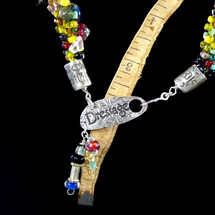 “Spirited Dressage Beaded Necklace” Overall length: 20", Clasp length: 2", Price: $550, Chisholm Ref. #: SBW-N9 | One-of-a-kind silver & beadwork necklace is woven using a multicolored “bead soup” made up of glass beads of many shapes and sizes. The end-caps are textured with many of the warm blood breed logos. The textured clasp declares, “Dressage,” while providing support for an asymmetrical tassel of beads. The findings are all handcrafted in .960 silver.