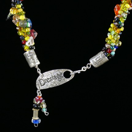 “Spirited Dressage Beaded Necklace” Overall length: 20", Clasp length: 2", Price: $550, Chisholm Ref. #: SBW-N9 | One-of-a-kind silver & beadwork necklace is woven using a multicolored “bead soup” made up of glass beads of many shapes and sizes. The end-caps are textured with many of the warm blood breed logos. The textured clasp declares, “Dressage,” while providing support for an asymmetrical tassel of beads. The findings are all handcrafted in .960 silver.