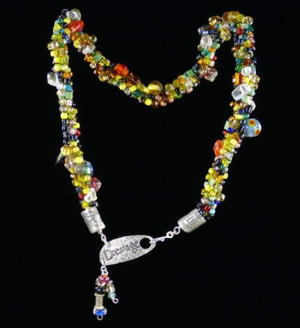 “Spirited Dressage Beaded Necklace” Overall length: 20", Clasp length: 2", Price: $550, Chisholm Ref. #: SBW-N9 | One-of-a-kind silver & beadwork necklace is woven using a multicolored “bead soup” made up of glass beads of many shapes and sizes. The end-caps are textured with many of the warm blood breed logos. The textured clasp declares, “Dressage,” while providing support for an asymmetrical tassel of beads. The findings are all handcrafted in .960 silver.