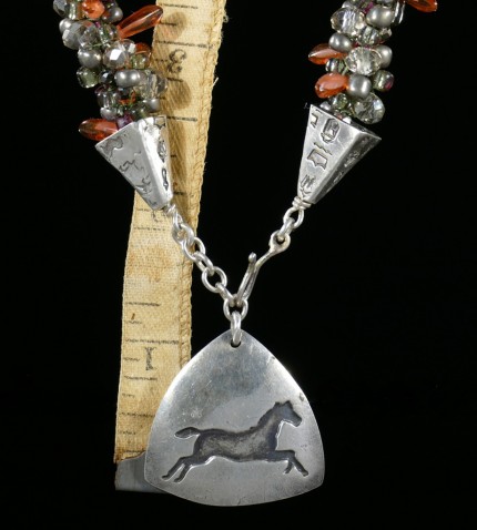 “Triple Luck Beaded Necklace” Overall length: 19", Pendant: 1.25" x 1.25", Price: $550, Chisholm Ref. #: SBW-N11 | One-of-a-kind silver & beadwork necklace made of freshwater pearls, Czech fire polished crystals, Czech glass dagger beads, and glass seed beads. The handmade, silver end-caps are textured with a motif of warmblood breed logos. The focal piece of the necklace is a convex, triangular pendant with the dramatic silhouette of a running horse. The findings are all handcrafted in .960 silver.